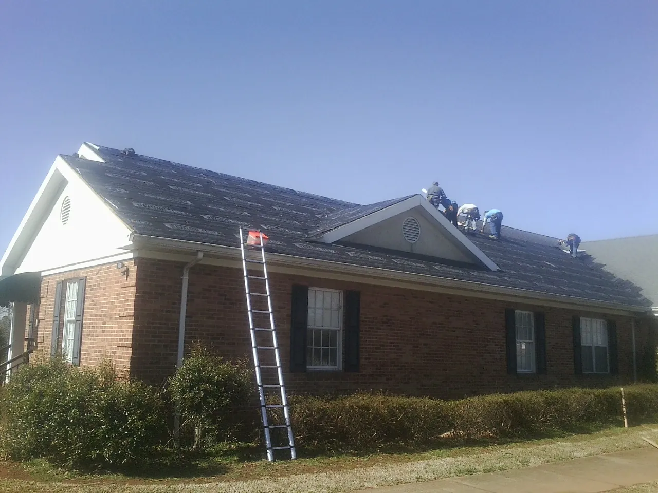 Crew tearing shingles off a brick ranch roof with a ladder set — Emergency Roof Repair work by our crew in Cambridge